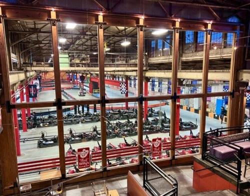 A spacious indoor go-kart track with multiple karts lined up, visible through large windows.