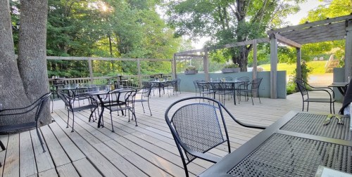 Outdoor dining area with black metal tables and chairs, surrounded by trees and greenery on a wooden deck.