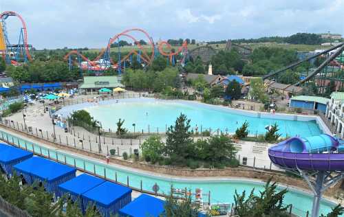 Aerial view of a water park featuring a large pool, lazy river, and roller coasters in the background.