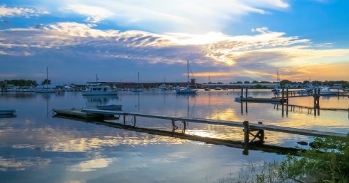 A serene marina at sunset, with boats docked and colorful clouds reflecting on the calm water.