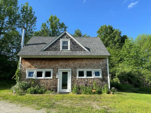 A charming wooden house with a sloped roof, surrounded by greenery and blue skies.