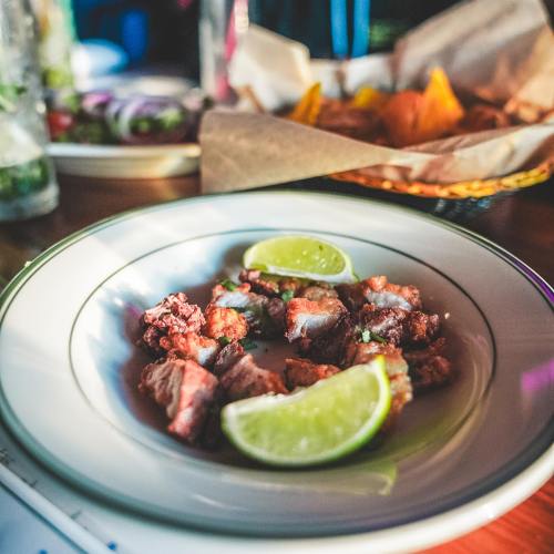 A plate of diced meat garnished with lime wedges, with chips and salad in the background.