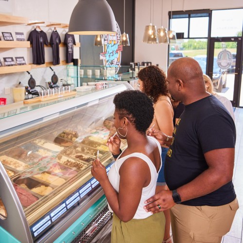 A group of people enjoying ice cream at a shop, looking at various flavors in a display case.