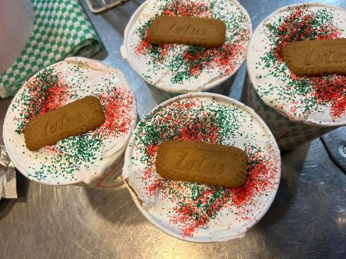 Four cups of dessert topped with whipped cream, red and green sprinkles, and a Lotus cookie.