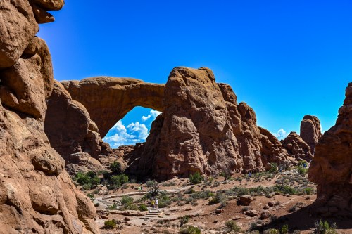 A natural stone arch surrounded by rugged rock formations and a clear blue sky in a desert landscape.