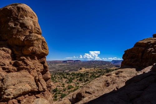 A panoramic view of a desert landscape with rocky formations under a clear blue sky and fluffy white clouds.