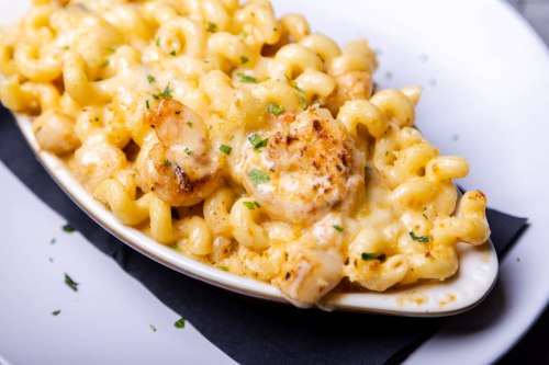 Creamy macaroni and cheese topped with grilled shrimp, garnished with parsley, served in a white dish.