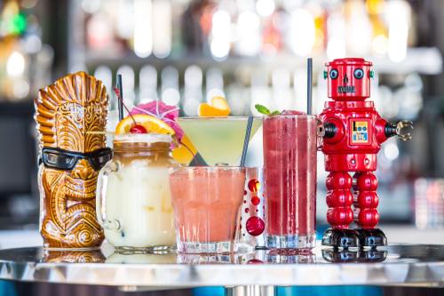 A colorful display of five cocktails, including a tiki mug, a mason jar, and a robot-shaped drink holder.