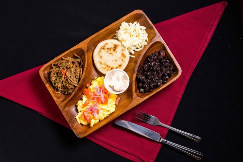 A wooden platter with shredded meat, scrambled eggs, cheese, black beans, a tortilla, and a dollop of sour cream.