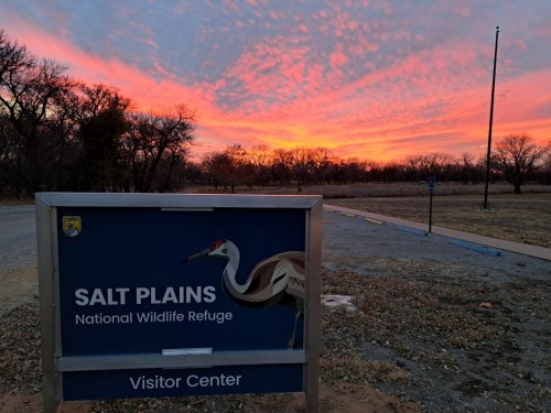 Sign for Salt Plains National Wildlife Refuge Visitor Center with a colorful sunset in the background.
