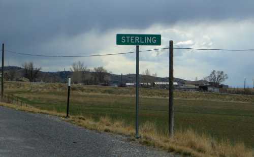 Green road sign reading "Sterling" with a rural landscape and cloudy sky in the background.