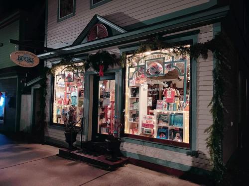 A cozy bookstore with festive decorations, warmly lit windows showcasing books and gifts.