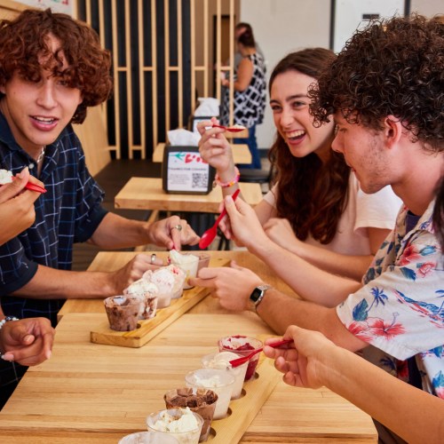 A group of friends enjoying ice cream together at a wooden table, smiling and sharing their treats.