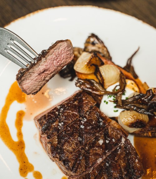 A perfectly cooked steak on a plate, accompanied by grilled onions and a rich sauce, with a fork holding a slice.