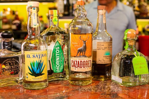 A variety of tequila bottles displayed on a bar counter, featuring brands like Don Julio, Hornitos, and Cazadores.