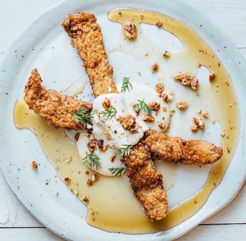 Fried strips on a plate drizzled with syrup, topped with granola and a dollop of cream, garnished with herbs.