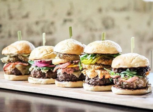 A lineup of five gourmet sliders on a wooden board, each with different toppings and ingredients.