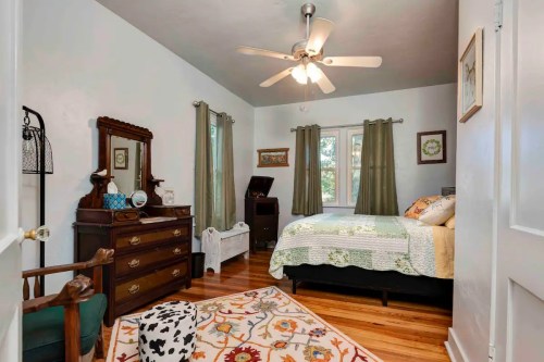 Cozy bedroom with a bed, dresser, mirror, and a patterned rug, featuring natural light from a window.