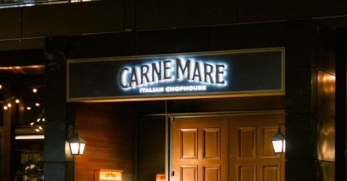 Sign for "Carne Mare Italian Chophouse" illuminated at night, with a wooden door and outdoor lighting.