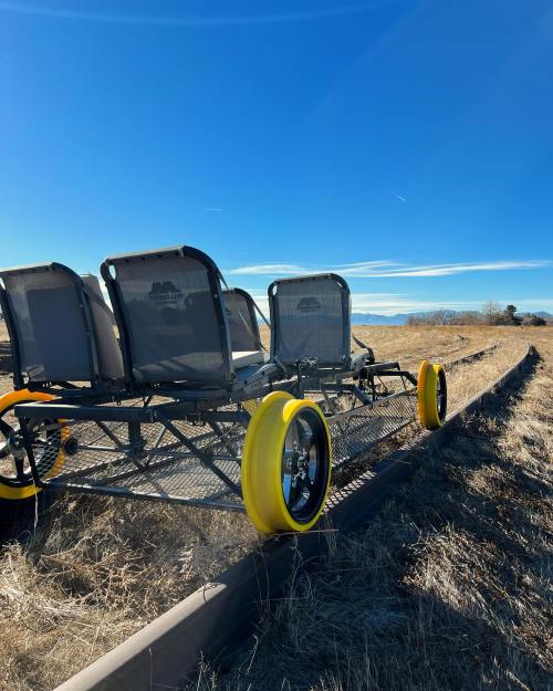 A three-seater cart with large yellow wheels parked on a grassy area under a clear blue sky.