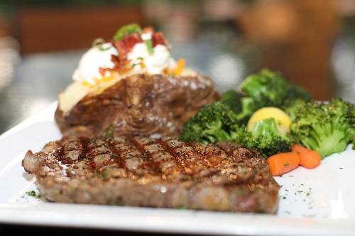 A plated meal featuring a grilled steak, baked potato with toppings, and a side of broccoli and carrots.