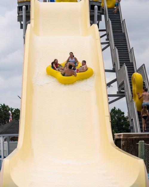A group of people on a yellow inflatable tube sliding down a large water slide at a water park.