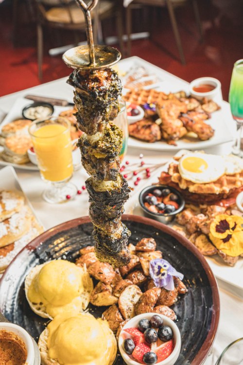 A vibrant spread of food featuring skewered meat, roasted potatoes, fruits, and colorful drinks on a dining table.
