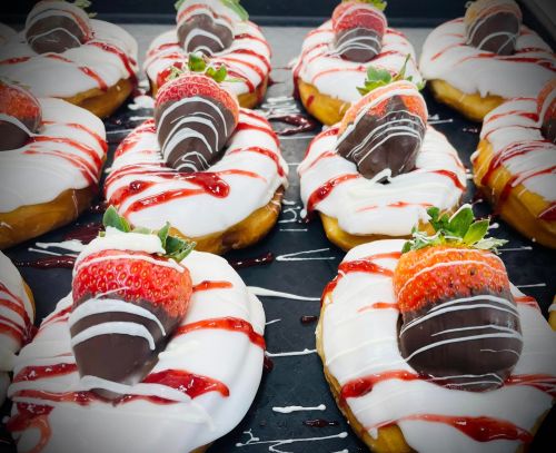 A tray of donuts topped with white icing, chocolate-covered strawberries, and strawberry drizzle.