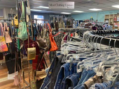 A thrift store interior filled with racks of clothing and bags, showcasing a variety of items for sale.