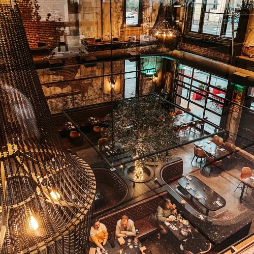 Aerial view of a stylish restaurant with modern decor, featuring a large chandelier and patrons dining at tables.