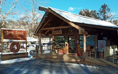 A rustic wooden building with a sign reading "Stoney Creek," surrounded by snow and trees on a sunny day.