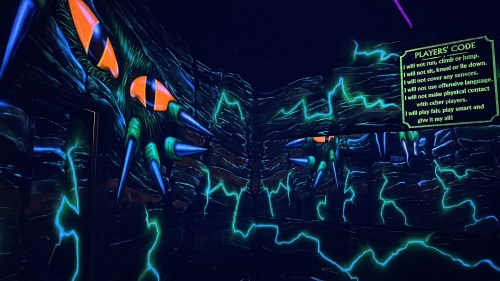 A dark room with neon spikes and lightning designs, featuring a "Player's Code" sign on the wall.