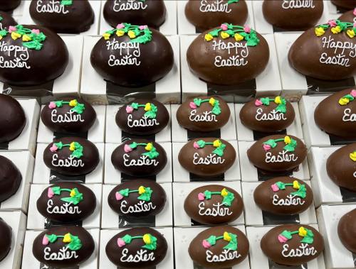 A display of chocolate Easter eggs, some decorated with "Happy Easter" and colorful flowers.