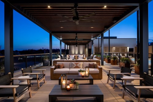 Modern rooftop lounge with comfortable seating, plants, and ambient lighting against a twilight sky.