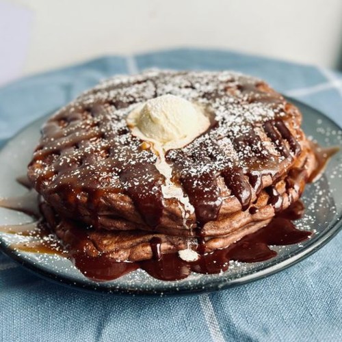 A stack of chocolate pancakes topped with a dollop of butter and drizzled with chocolate sauce, on a blue plate.