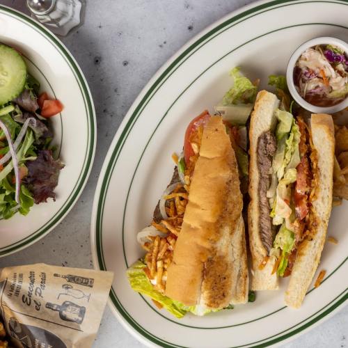 A plate with two sandwiches filled with meat and vegetables, accompanied by a small bowl of coleslaw and a side salad.