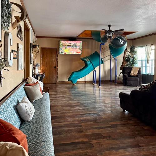 A spacious living room featuring a blue slide, a TV on the wall, and a cozy seating area with decorative pillows.