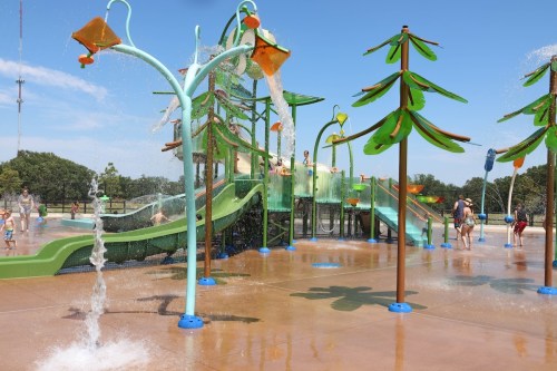 A colorful water play area with slides, fountains, and children playing under a clear blue sky.