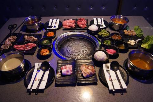A table set for a Korean BBQ meal, featuring various meats, sides, rice, and dipping sauces.