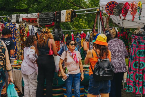 A vibrant market scene with people browsing colorful textiles and accessories under a sunny sky.