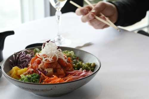 A colorful bowl of sushi salad with various vegetables, accompanied by a glass of wine and chopsticks.