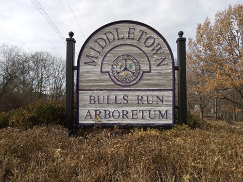 Sign for Middletown Bulls Run Arboretum, featuring a circular emblem and surrounded by autumn foliage.
