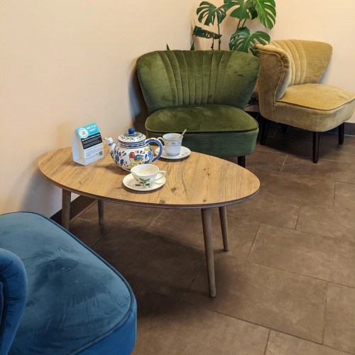 A cozy seating area with green and yellow chairs, a wooden coffee table, and a tea set on it.
