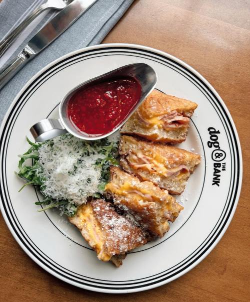 A plate with grilled cheese sandwiches, a side of greens, and a small bowl of raspberry sauce.