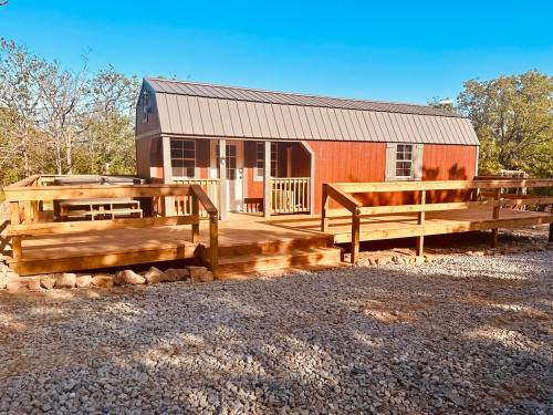A red cabin with a metal roof, surrounded by trees, featuring wooden decks and a gravel pathway.