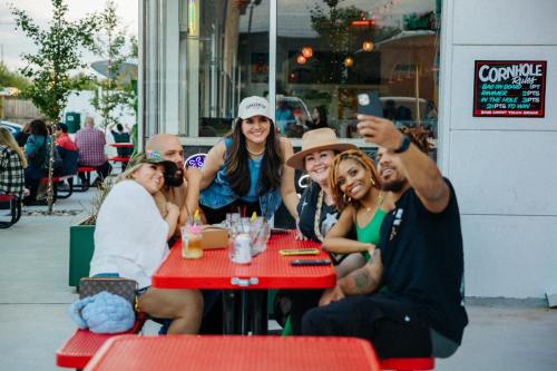 A group of friends smiling and taking a selfie at a colorful outdoor café with red tables.
