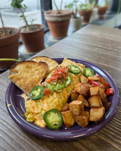A colorful plate featuring an omelette topped with tomatoes and jalapeños, served with toast and seasoned potato wedges.