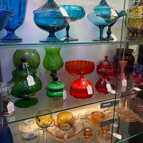 A display of colorful glassware, including vases and bowls, in various shapes and sizes on a glass shelf.