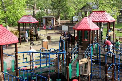 A vibrant playground with colorful structures, children playing, and adults supervising in a green park setting.