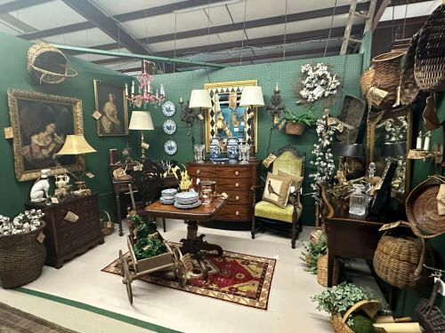 A cozy vintage display featuring furniture, decor, and antiques against a green backdrop in a market setting.